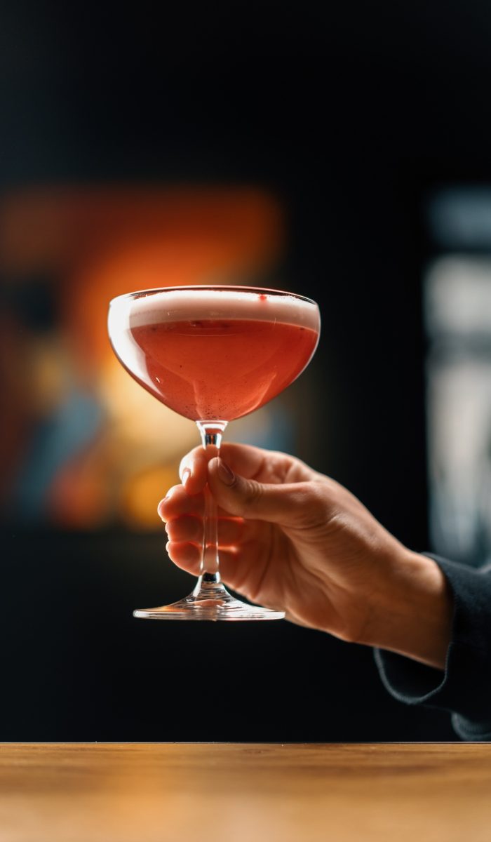customer holding delicious pink freshly made raspberry milk punch cocktail in hand bar